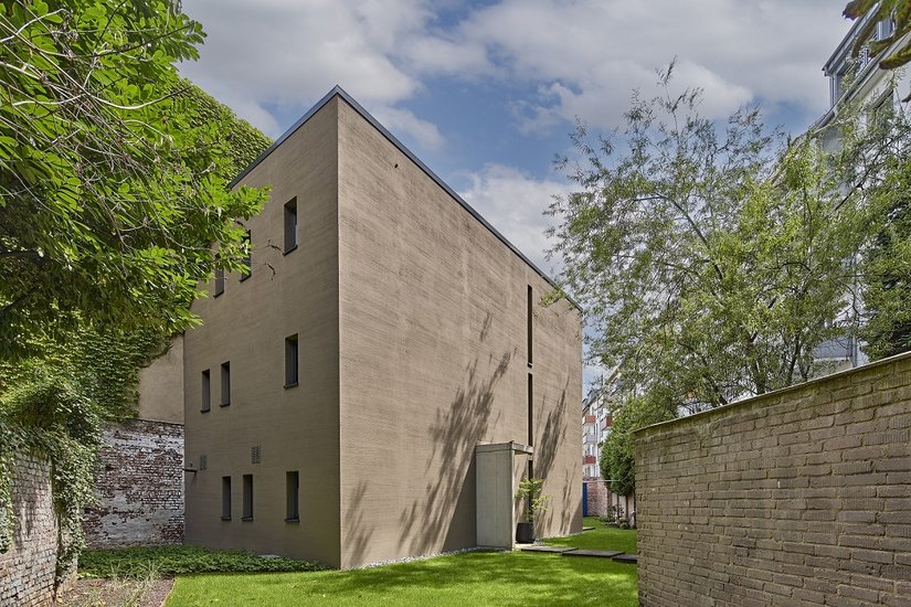 Auf einem verwinkelten „Restgrundstück“ inmitten der Stadt wurde das allgegengewärtige Platz- und Wohnungsproblem vorbildlich gelöst. An der wohl proportionierten monolithischen Westseite, die nur mit Türelement und Lichtfugen auskommt, spielt die Fassadengestaltung die Hauptrolle.