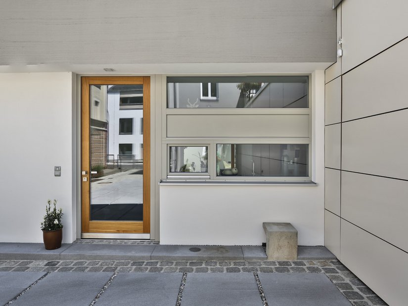 Das helle Holz der Haustür setzt sich deutlich vom einheitlichen Grau ab.