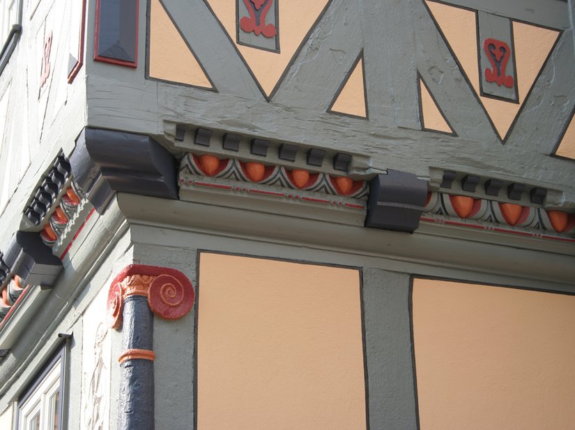 Die ocker-orangefarbene Gefachefarbigkeit nimmt die ortstypische Farbigkeit der Begleitstriche in abgewandelter Form wieder auf, integriert das Gebäude ins Gesamtensemble und ihm die ihm gebührende Wertigkeit und Betonung innerhalb des Innenstadtbereiches.