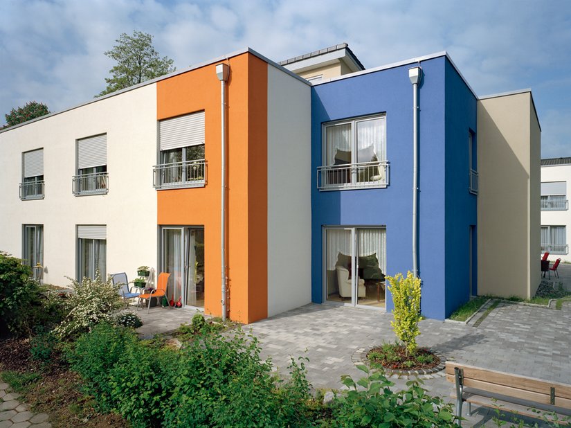 Das satte Orange und das gedämpfte Blau bringen die ansonsten in weiß und vanillefarbig gestaltete Gebäudehülle zum Leuchten. Die gestaffelte Architektur, ihre Kuben und die Dimension werden erlebbar.