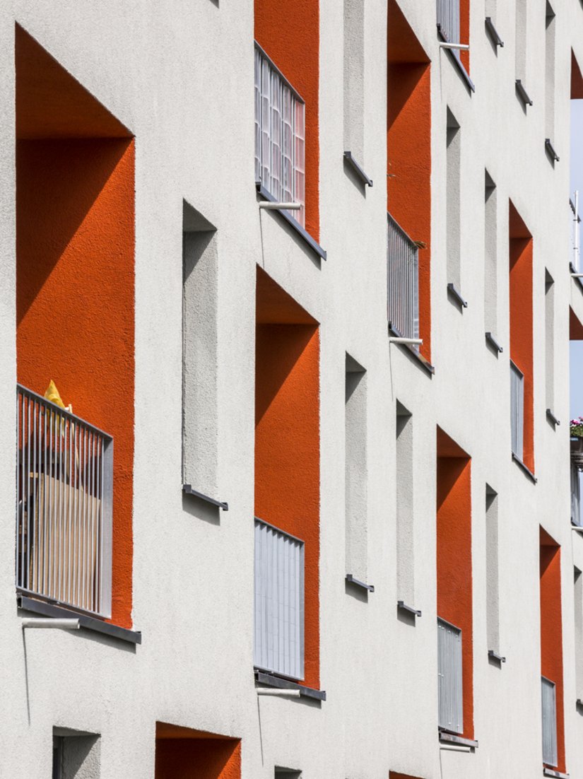 Die hellgraue Fassade wird durch markante orangerote Loggien unterbrochen.