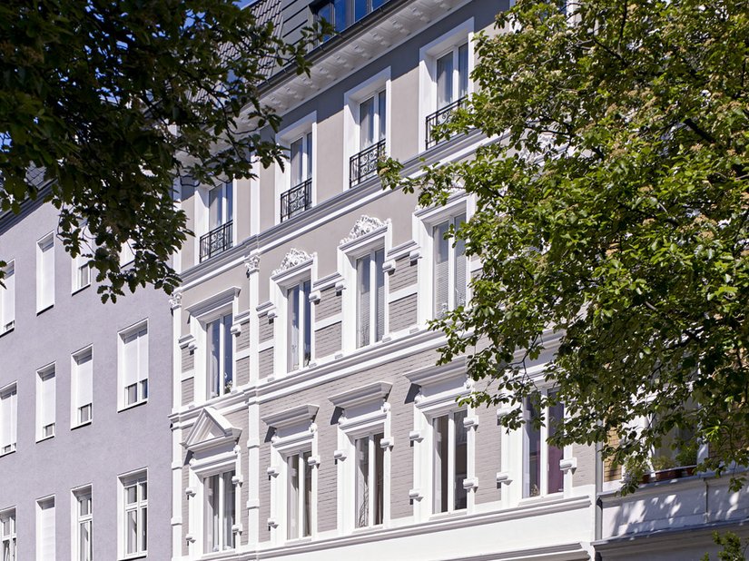Die Stilfassade erstrahlt in einem warmen, den Farbton Taupe ähnlichen Grauton. Die stark gegliederten und verzierten Fenstergewände sind in Weiss gefasst.