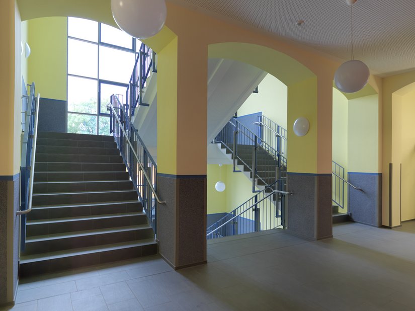 Das Treppenhaus erhält durch die großen Fenster und den warmen Gelbton viel Helligkeit.